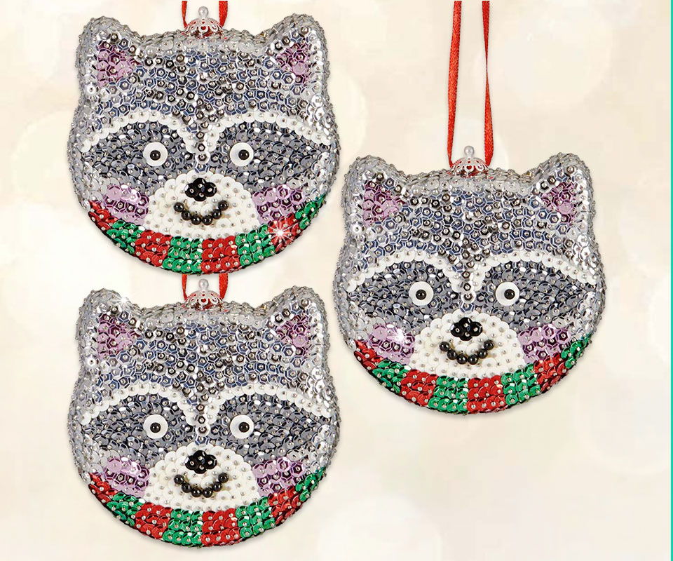 Three raccoon face ornaments with colorful scarves, hanging on red ribbons.