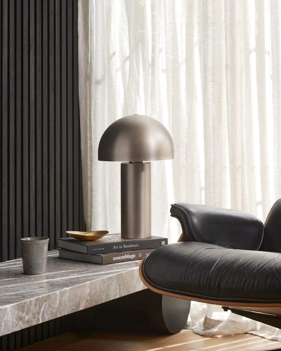 Modern interior with a table lamp, books, and a black chair.