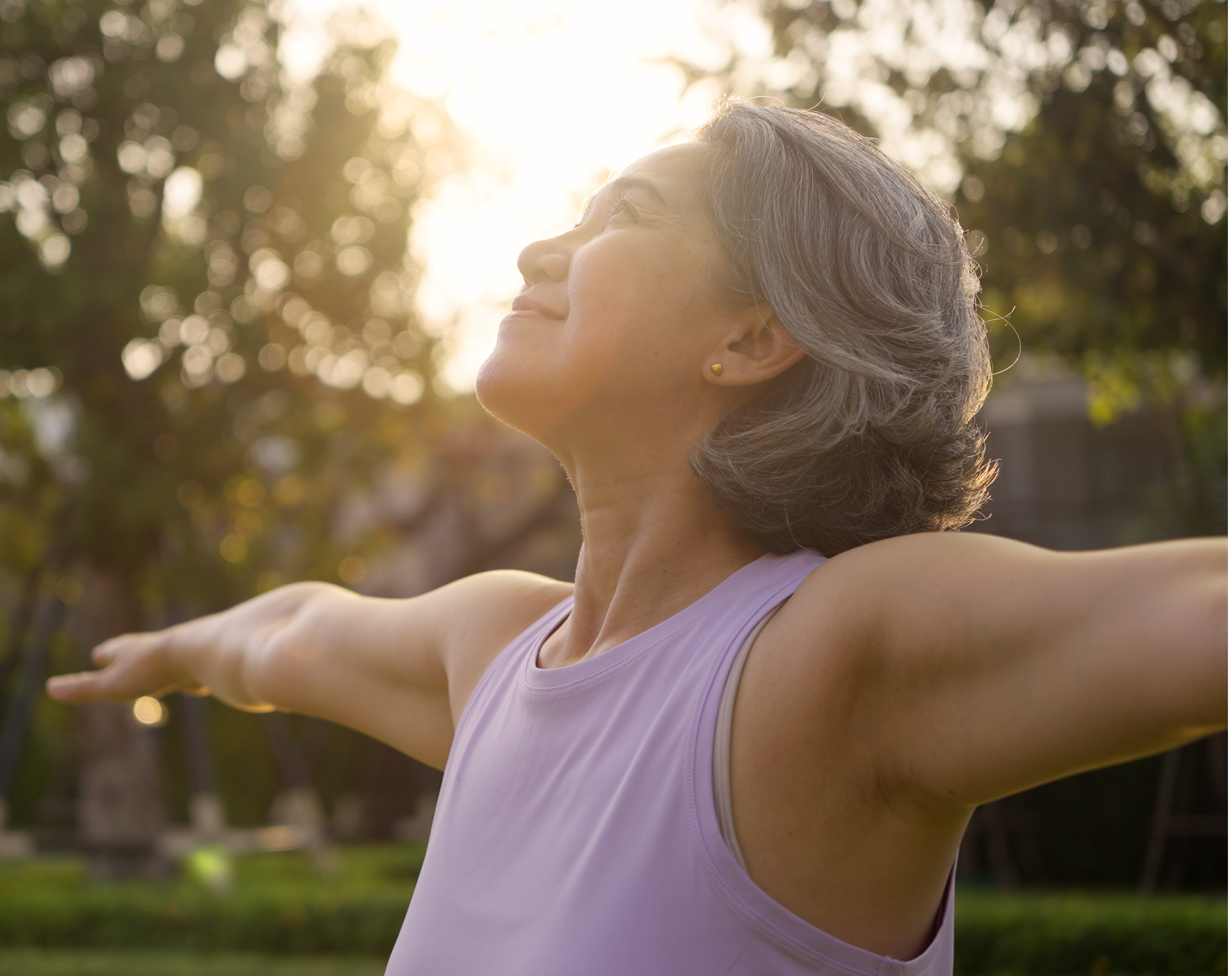 Woman with gray hair enjoying nature, arms outstretched, during sunset.