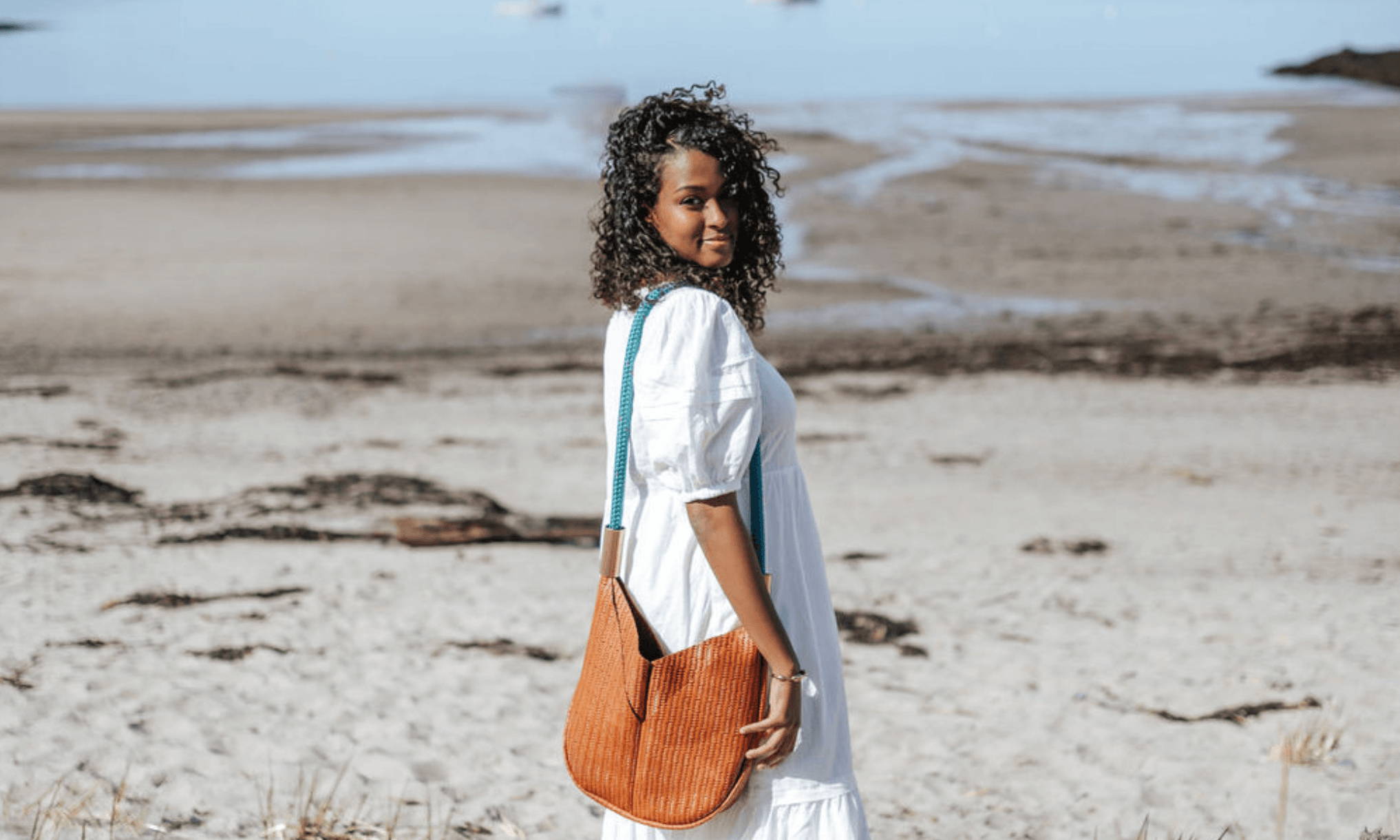 woman wearing a brown crossbody bag with teal rope on the beach