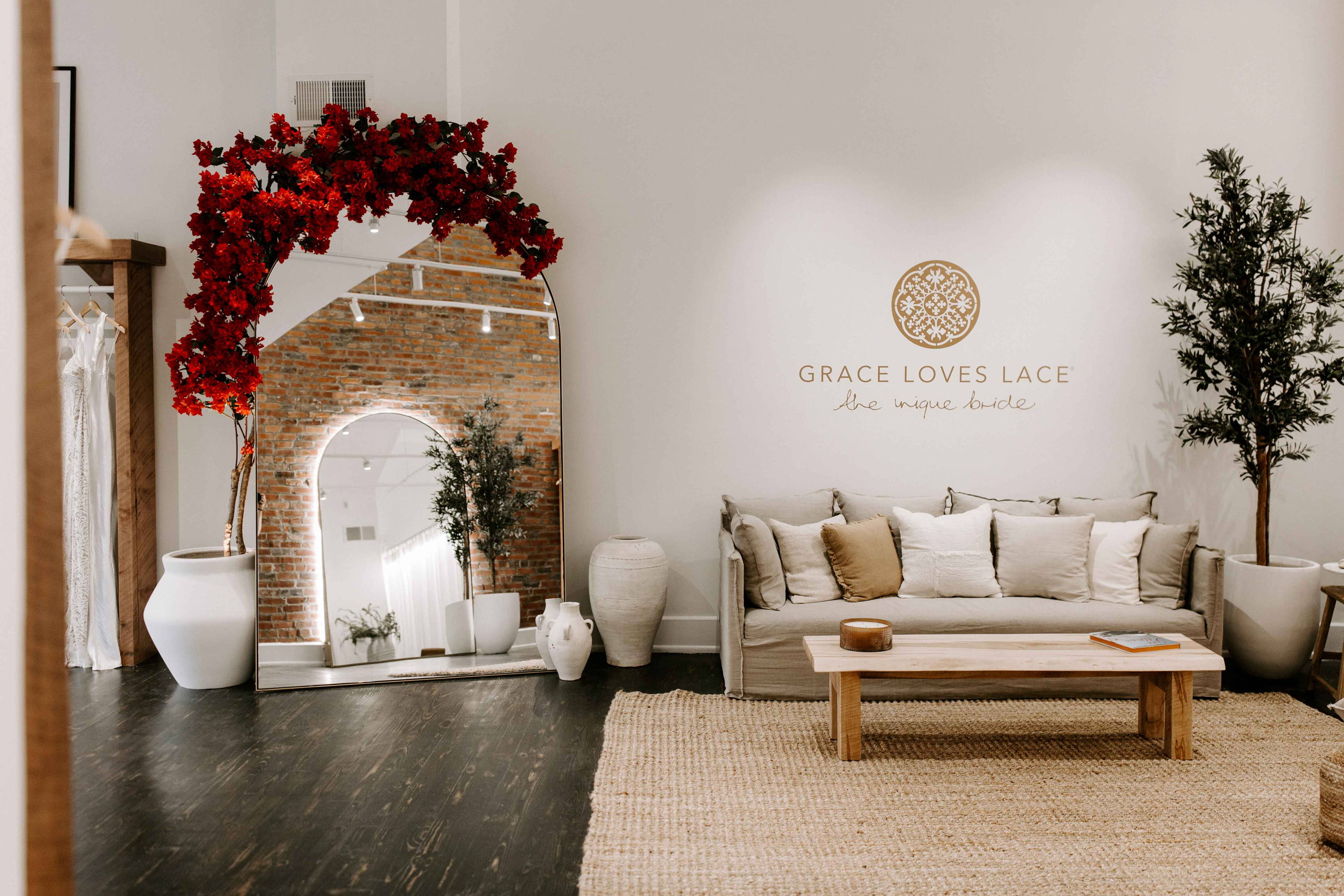 Beigefarbene Couch, rotes Blumenarrangement auf dem Spiegel und Grace Loves Lace-Logo auf weißer Wand