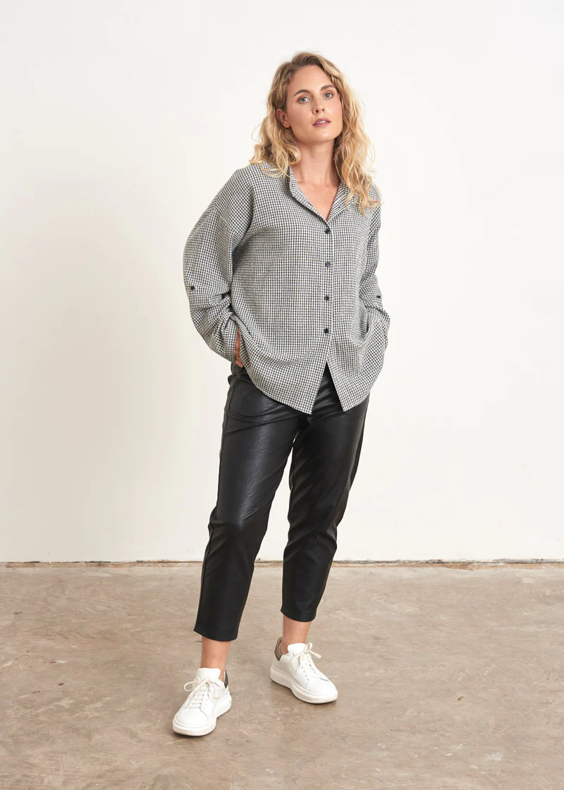 A model wearing a black and white checkered shirt with faux leather black trousers and white trainers