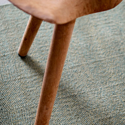 A wooden chair leg on a textured green rug.