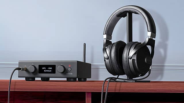 A headphone and amplifier setup on a wooden table against a blue wall.