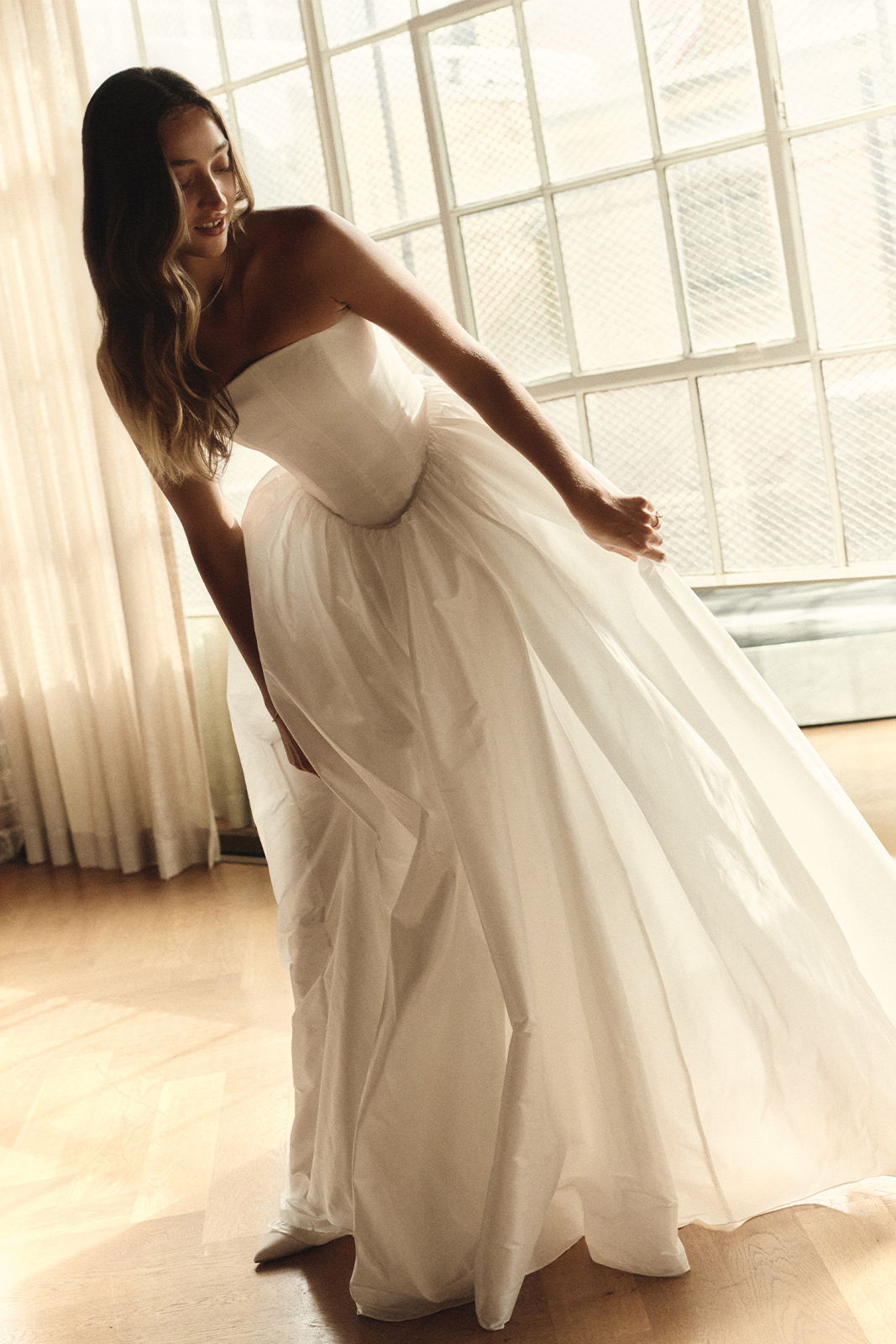Woman in a strapless white dress posing by a window.
