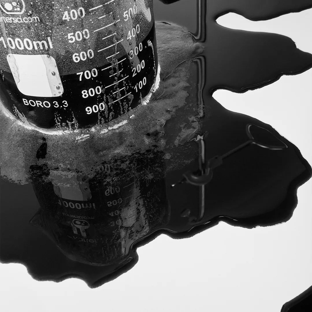 Beaker with liquid spilling onto a surface, in black and white.