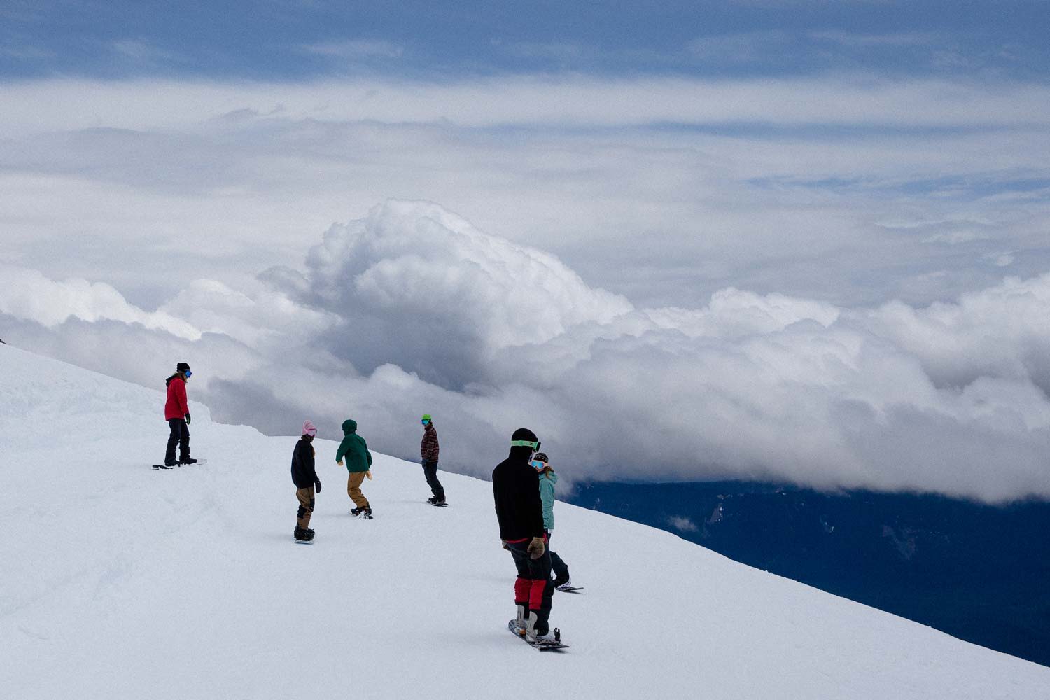 People snowboarding on a snowy mountain ridge with clouds in the background.