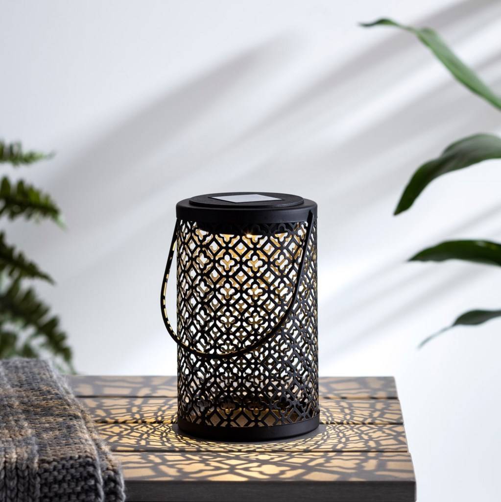 Black solar lantern on a wooden table in a cosy setting.