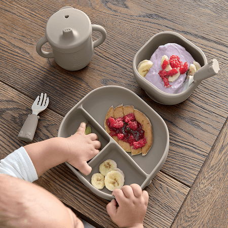 A child reaching for food in a divided plate on a wooden table.