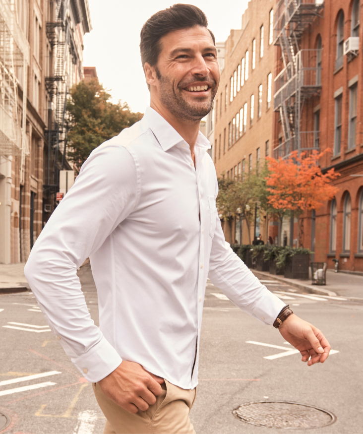 Smiling man walking on a city street in a white shirt.
