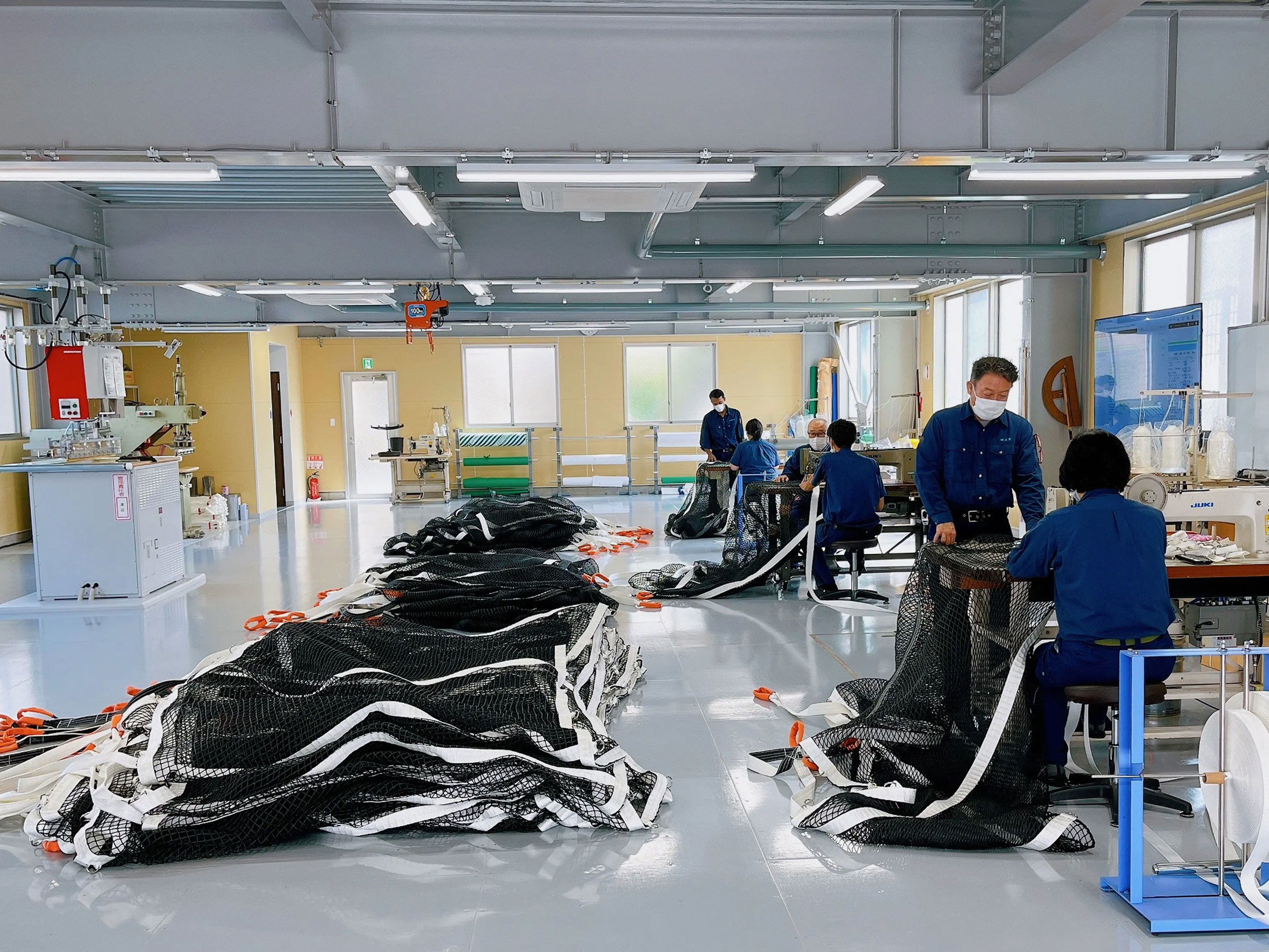 Workers in a spacious room assembling or repairing equipment with black materials.