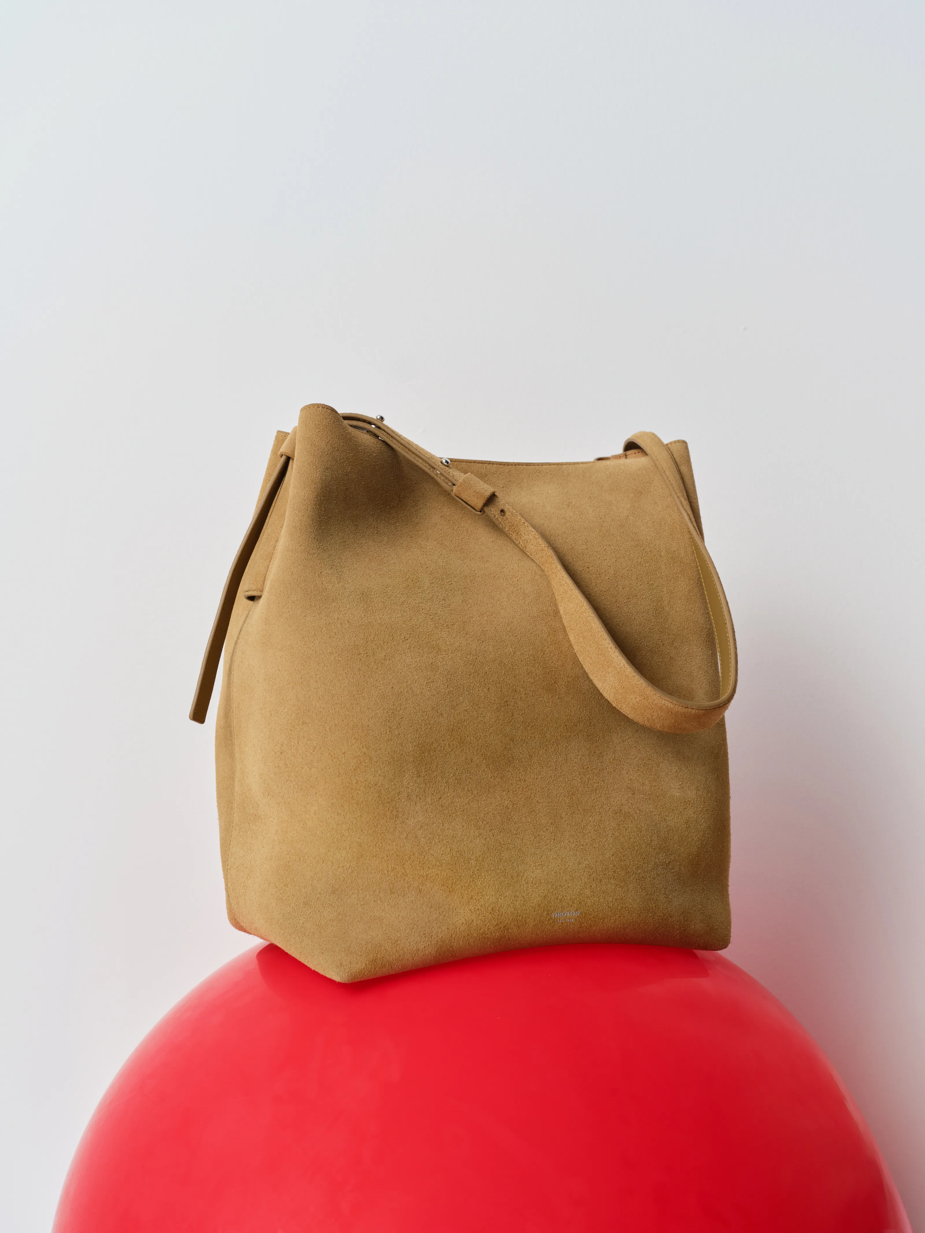 Brown suede bag resting on a red spherical surface.