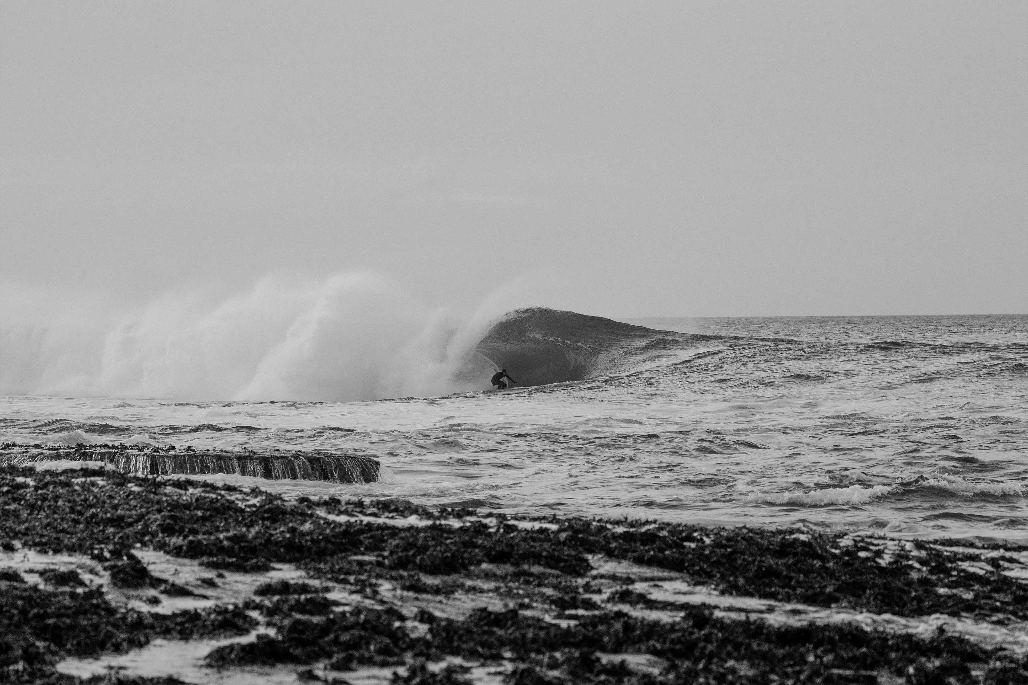 Black and white image of ocean waves crashing on rocky shore.
