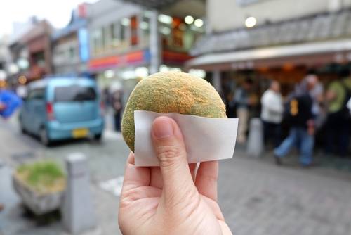 Hand holding a matcha mochi covered in soybean powder