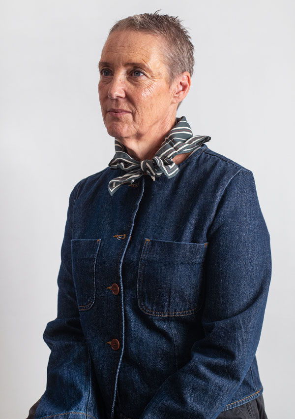 Victoria wearing a denim jacket and scarf, seated against a white background.