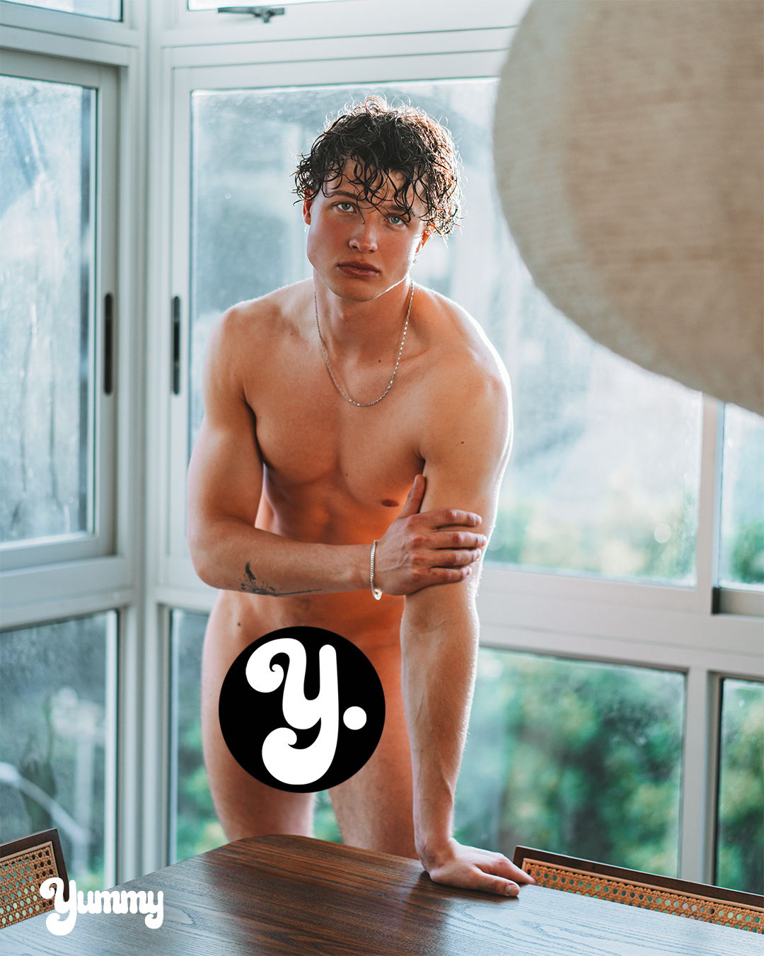 Young man posing by a window in a casual setting.