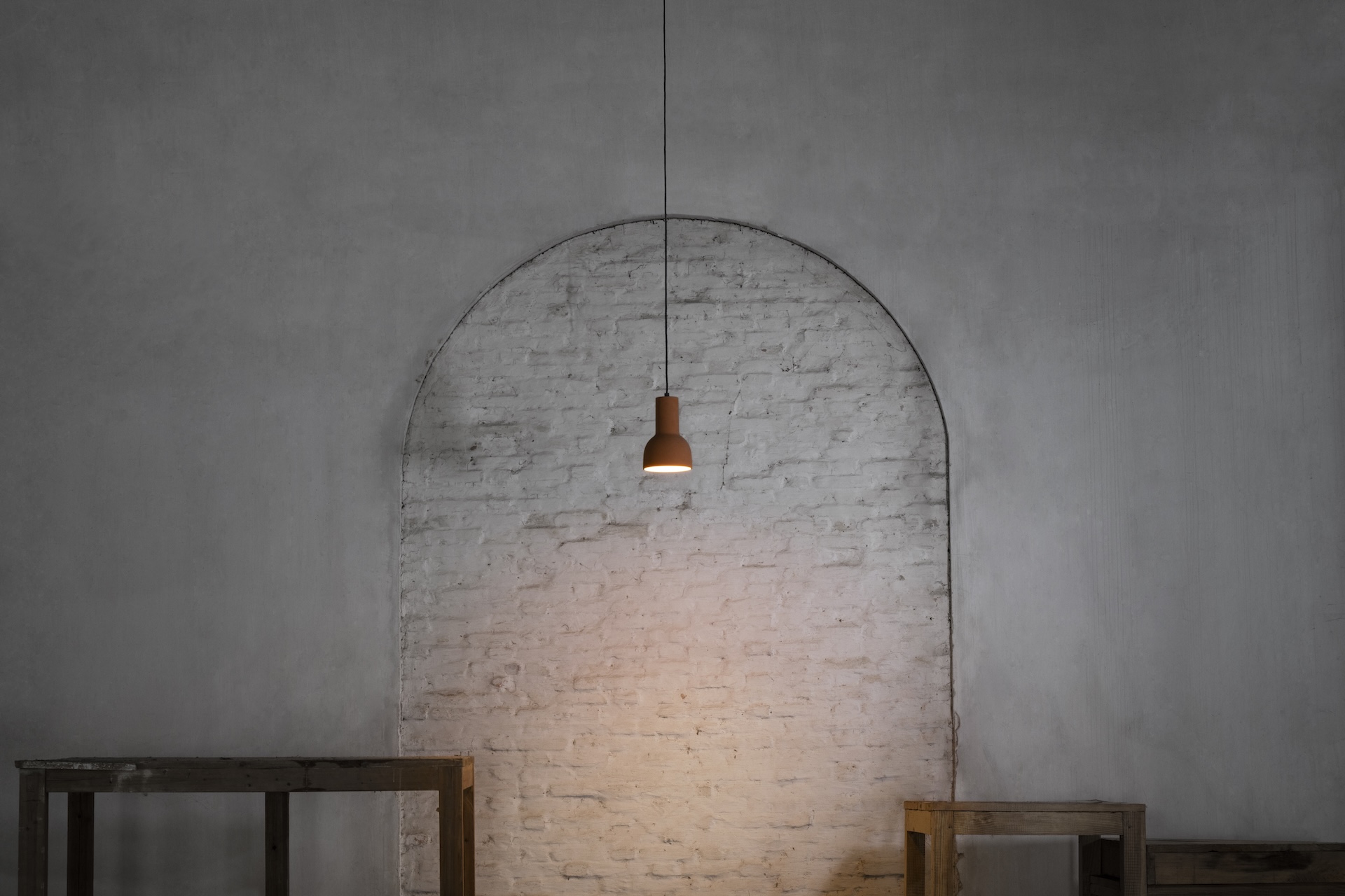 A hanging light fixture against a textured wall with wooden frames below.