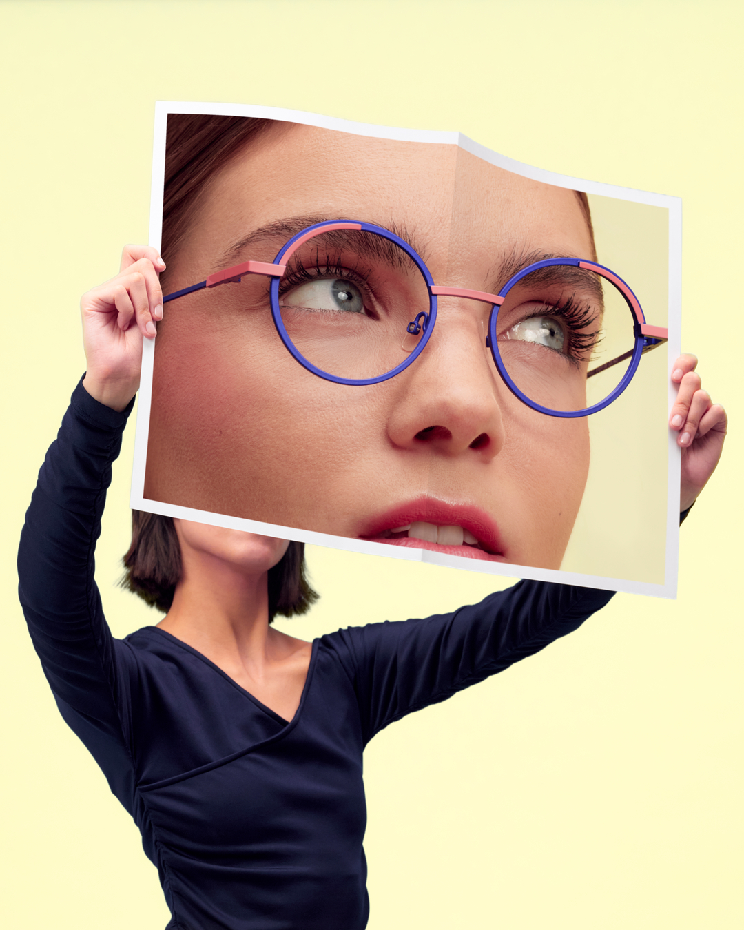 Person holding a large photo of a woman's face with face a face glasses.