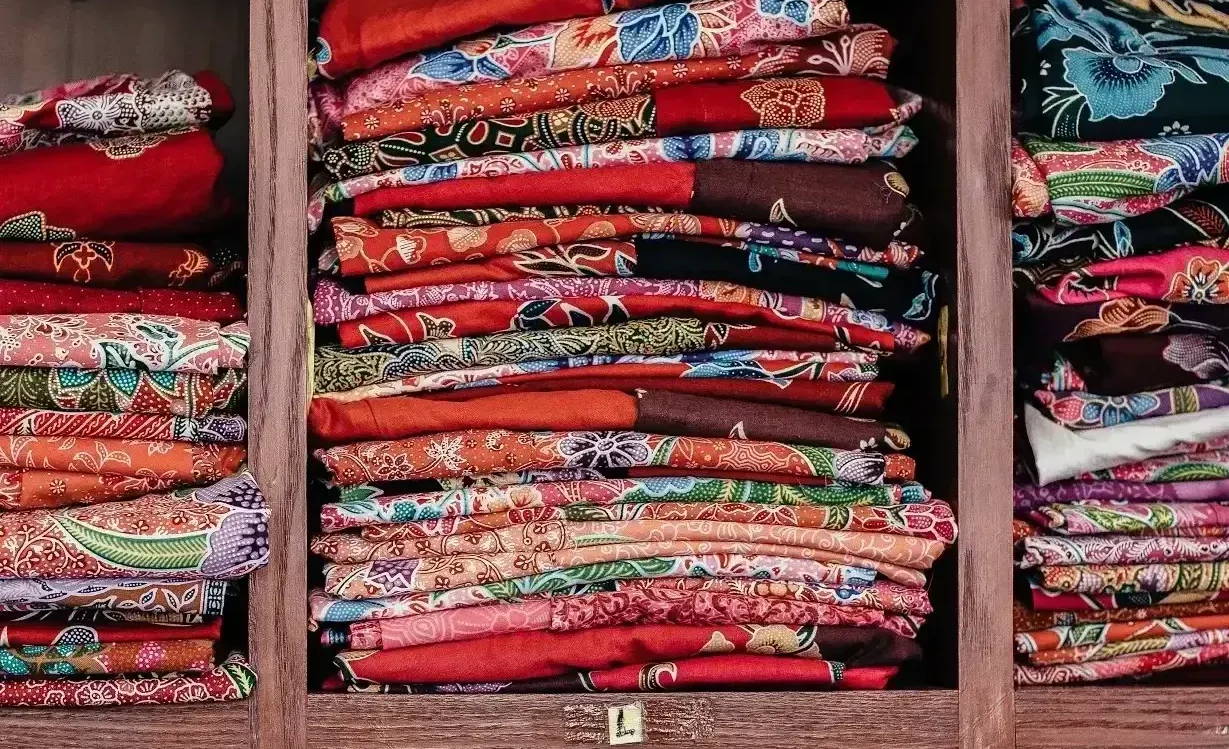 Stacks of differently patterned fabric sit on wooden shelves.