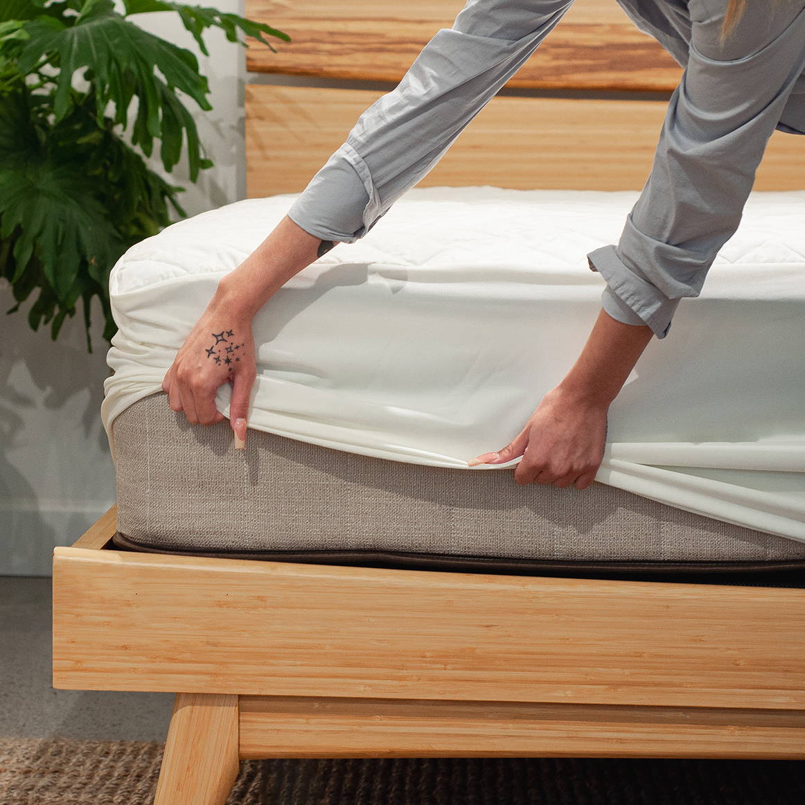 a person pulling a mattress protector over the corner of an owl natural latex hybrid mattress