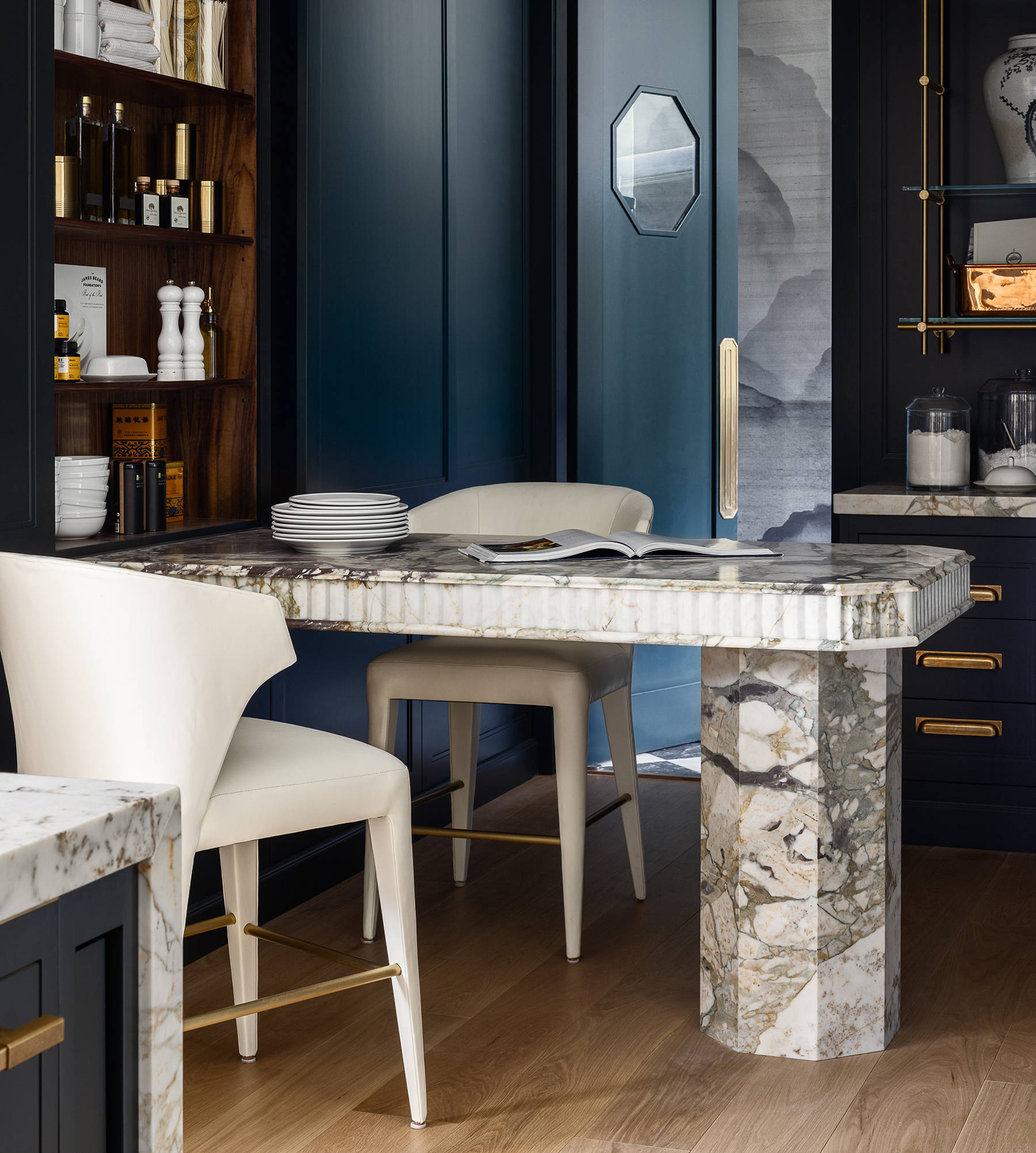 Kitchen with navy units, walls and door, wooden floor, marble table and white chairs. Design by McCroskey Interiors. 
