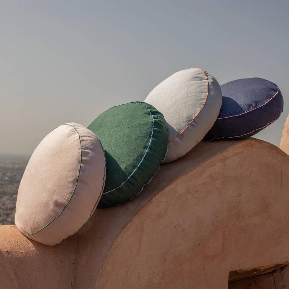 A stack of four different coloured round linen cushions on top of a terracotta coloured archway in Jaipur.