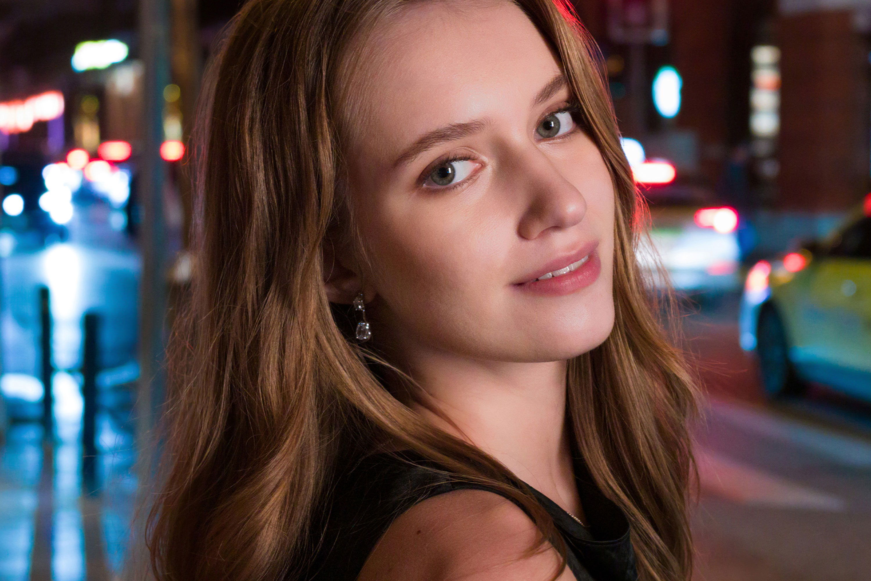 Woman with long hair smiling in a city at night.