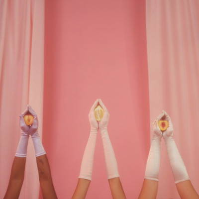 Fotografia de três pares braços e mãos com luvas brancas, seguram em formato de concha frutas cortadas ao meio