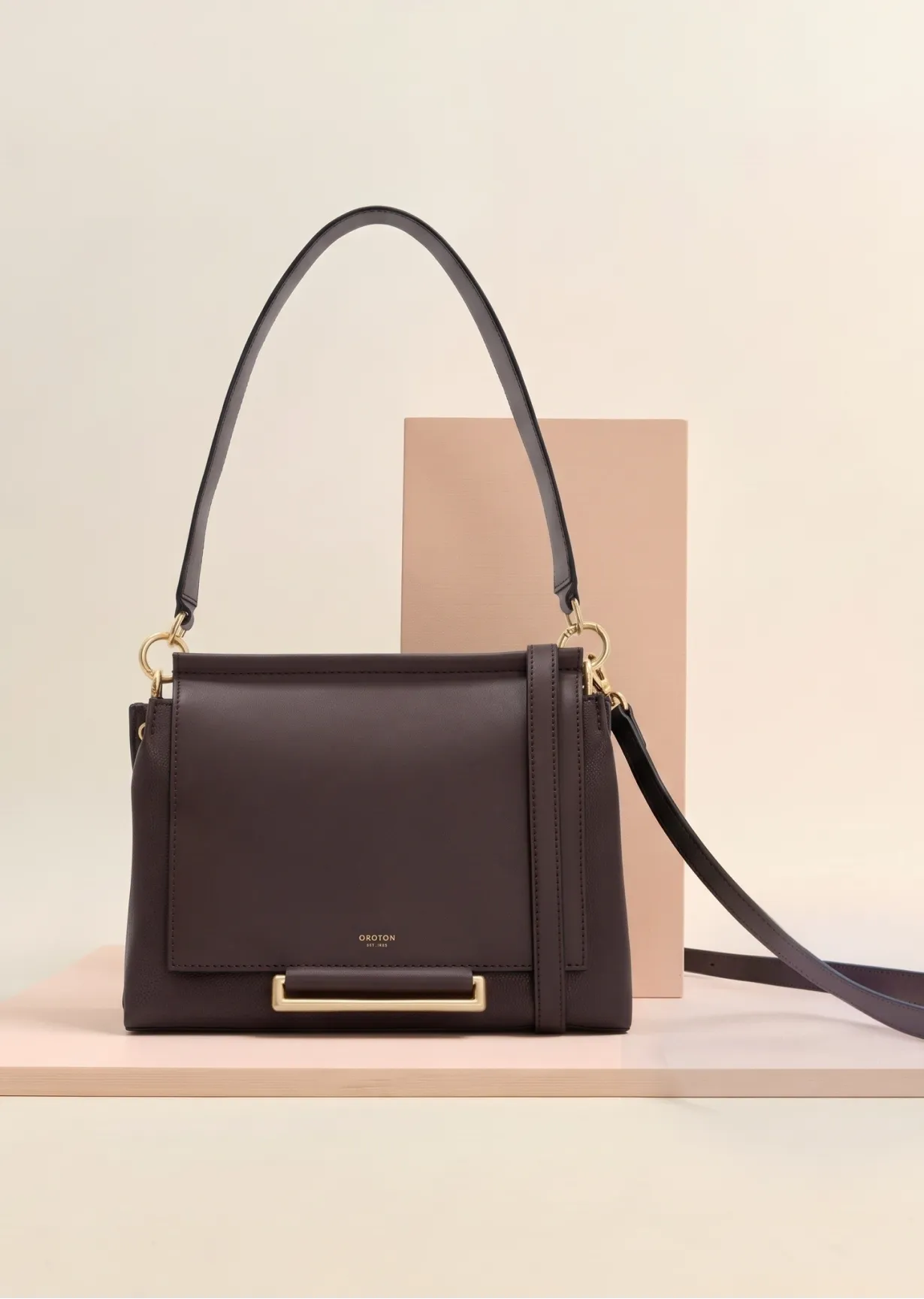 Brown handbag with a shoulder strap on a pastel background.
