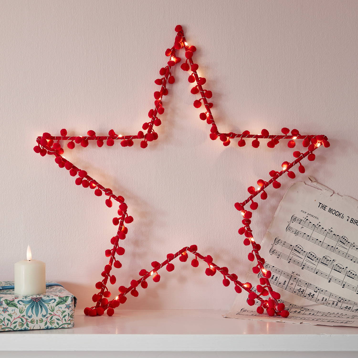 Red pom pom star light on a shelf with an LED candle