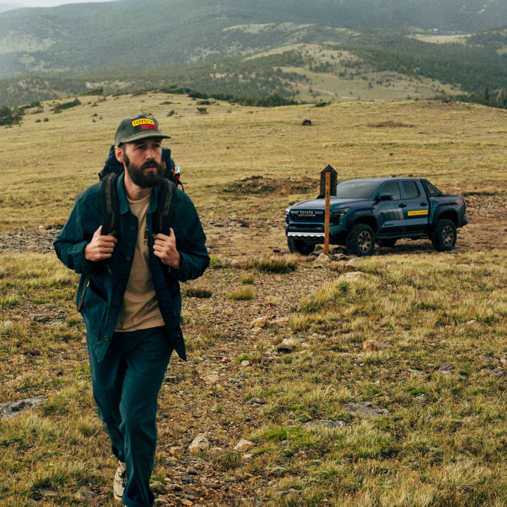 A man hiking in a grassy field near a parked truck.