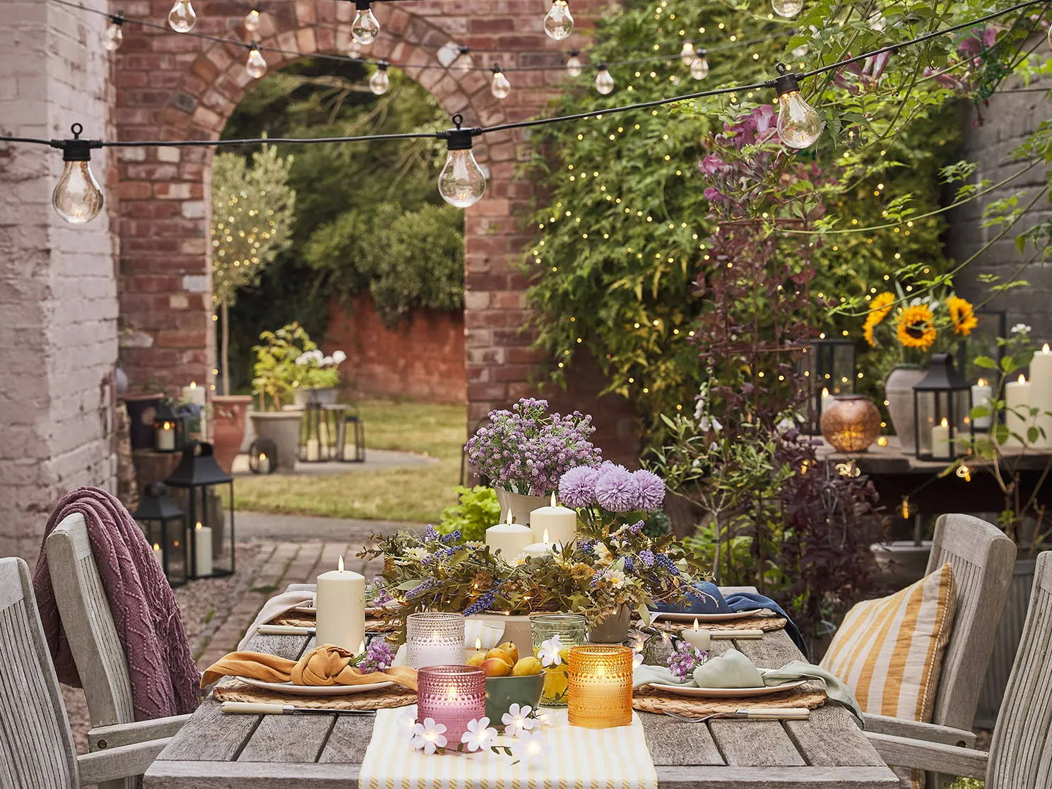 A summer alfresco dinning setting with LED candles, lanterns, festoon lights and lanterns. 