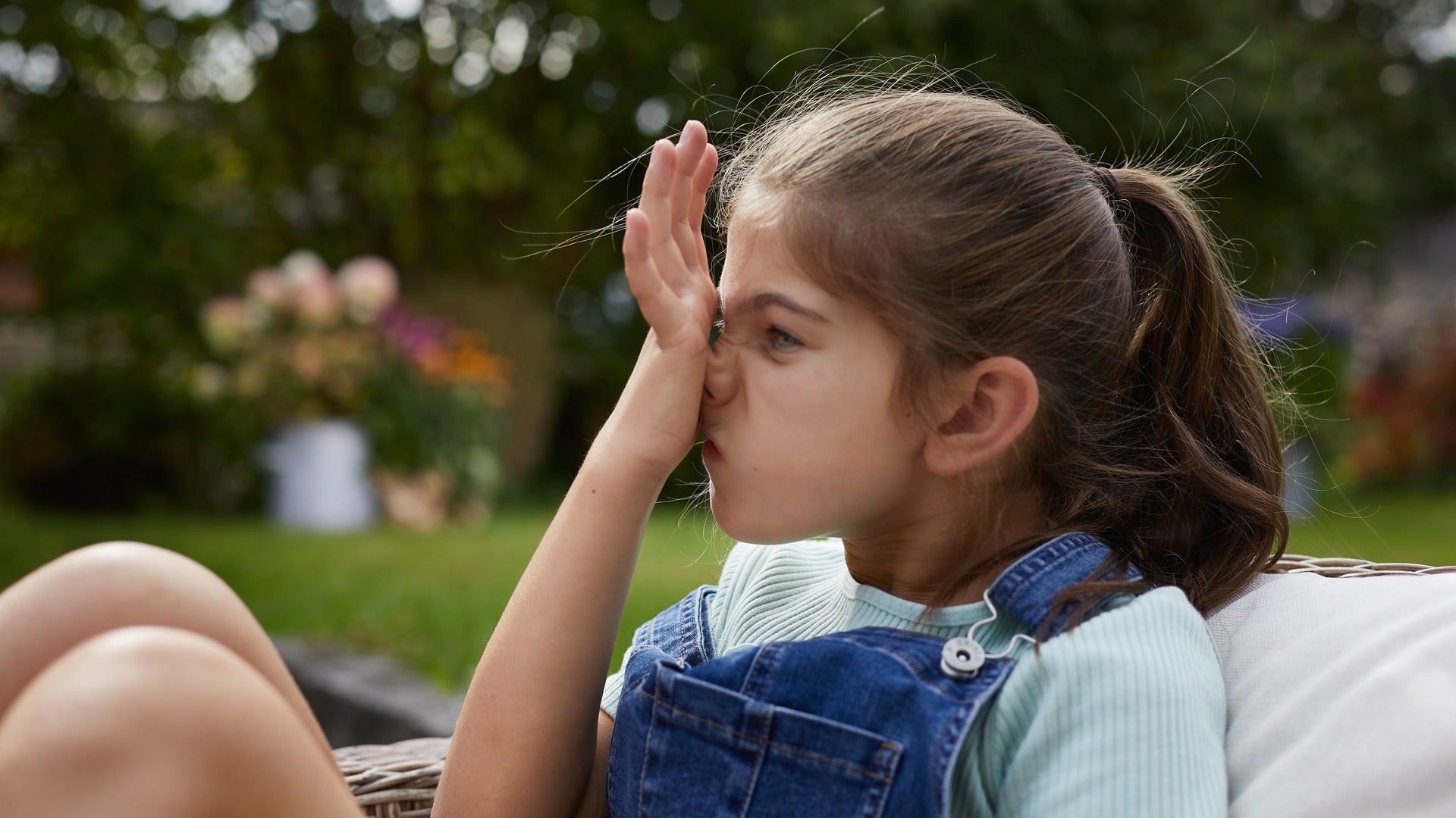 Girl with seasonal allergies sat in the garden rubbing her itchy nose upwards with her palm - it’s called the allergic salute