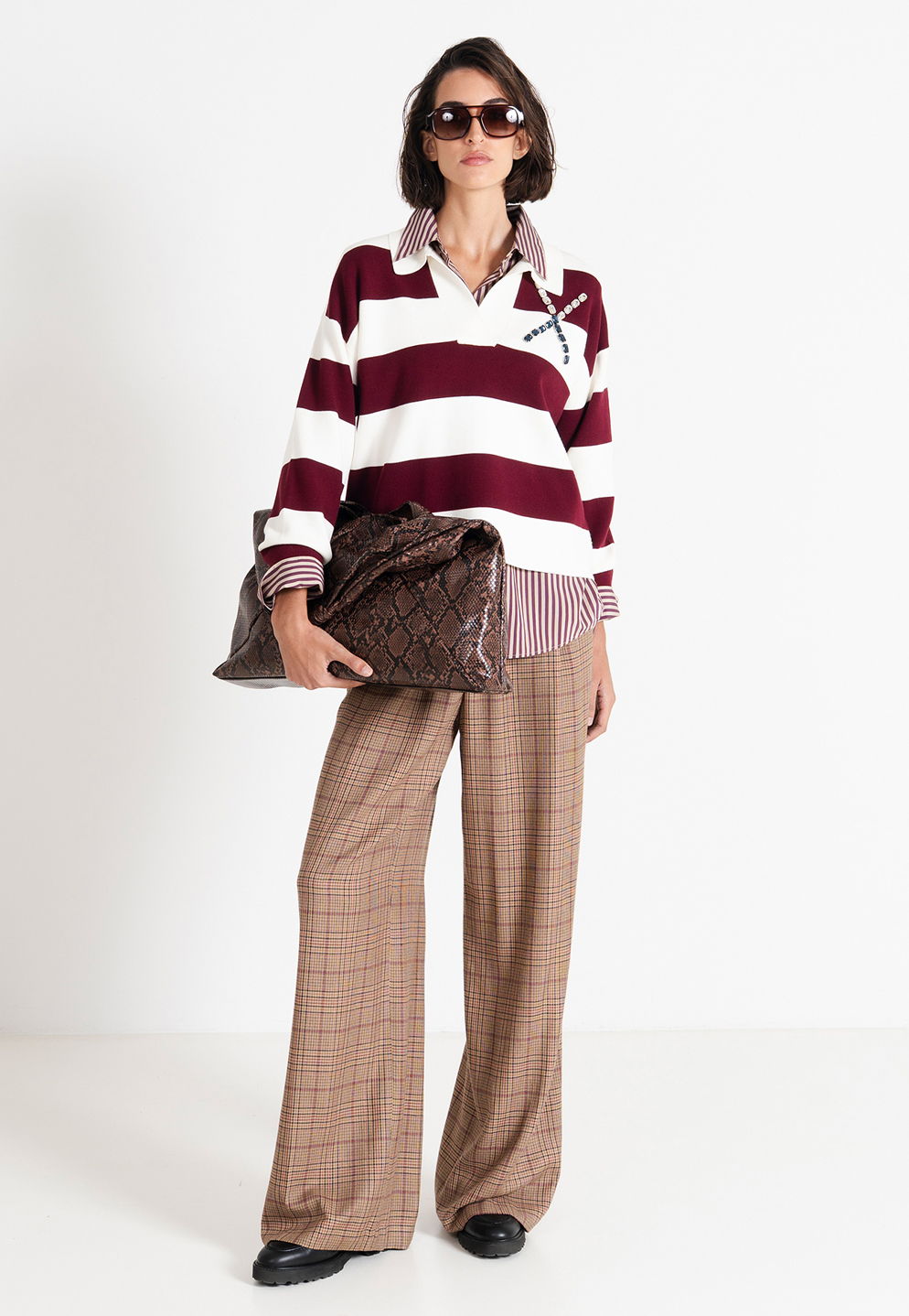 Person wearing striped sweater and plaid pants, holding a large bag.