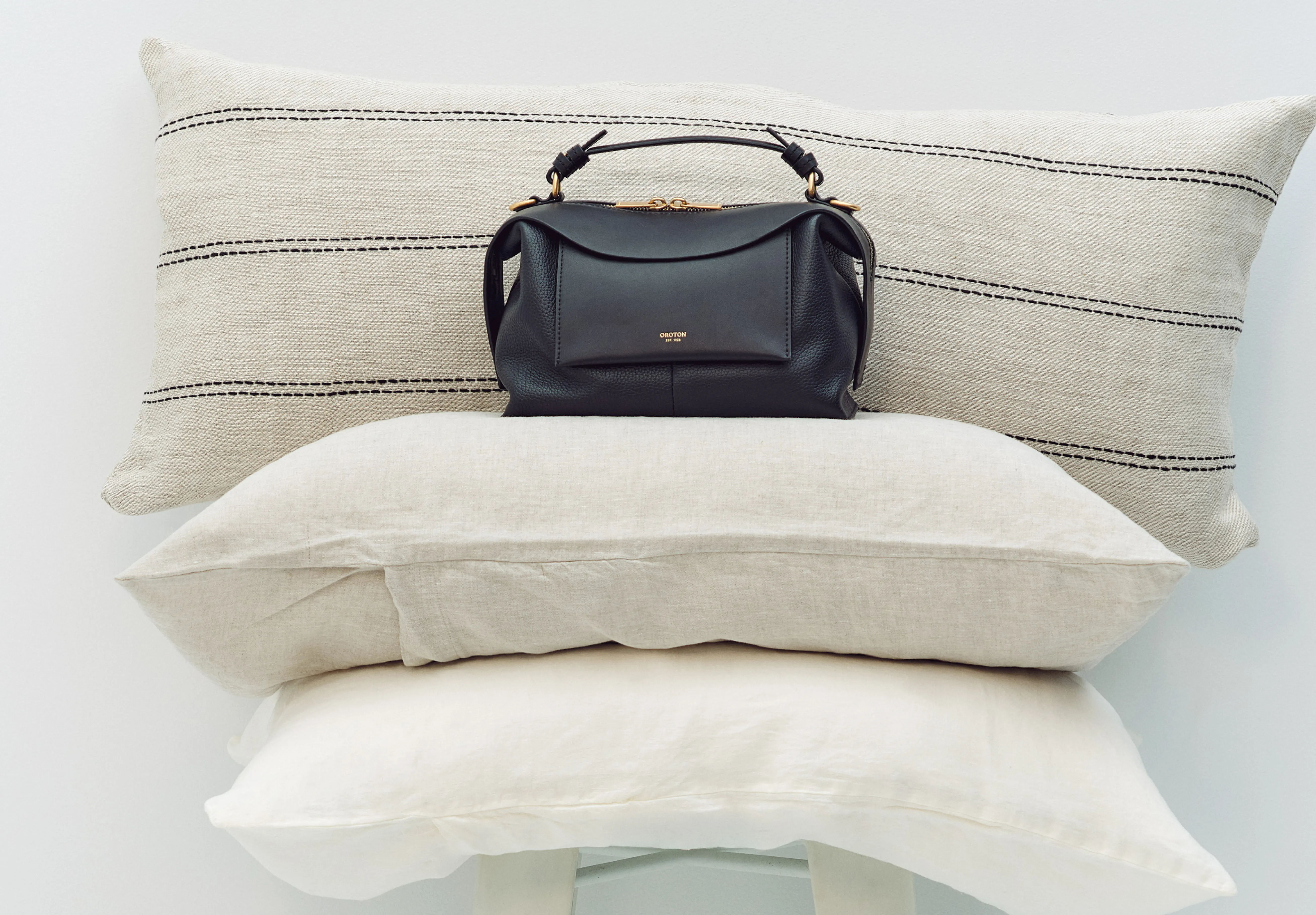 A black handbag placed on stacked decorative pillows.