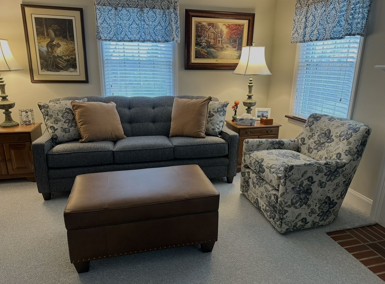 Living room with a sofa, armchair, coffee table, and window views.