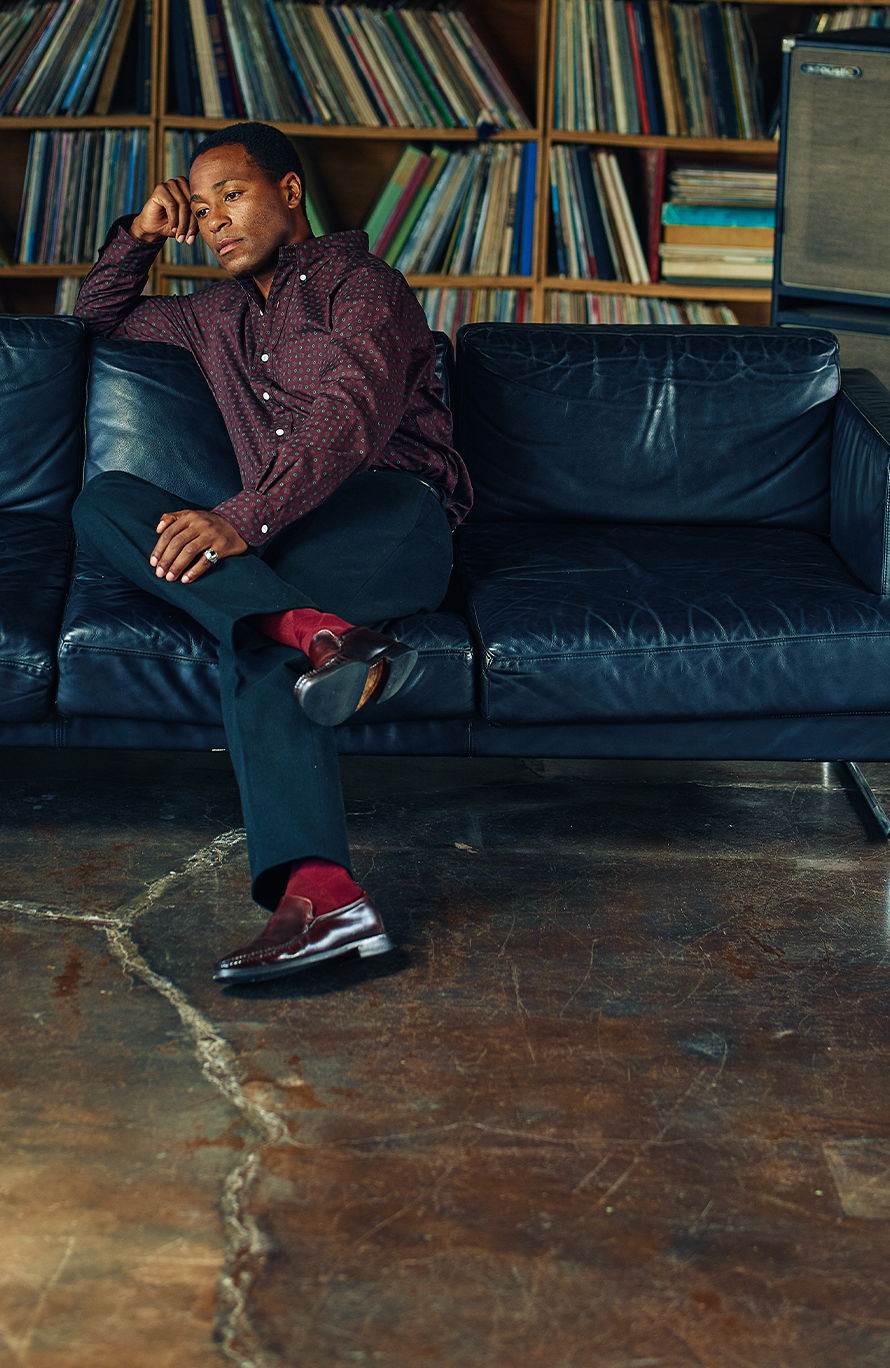 A man sitting on a couch surrounded by records in a cozy room.
