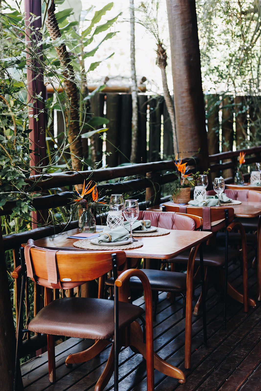 Dining area with wooden tables, chairs, and tropical greenery in the background.