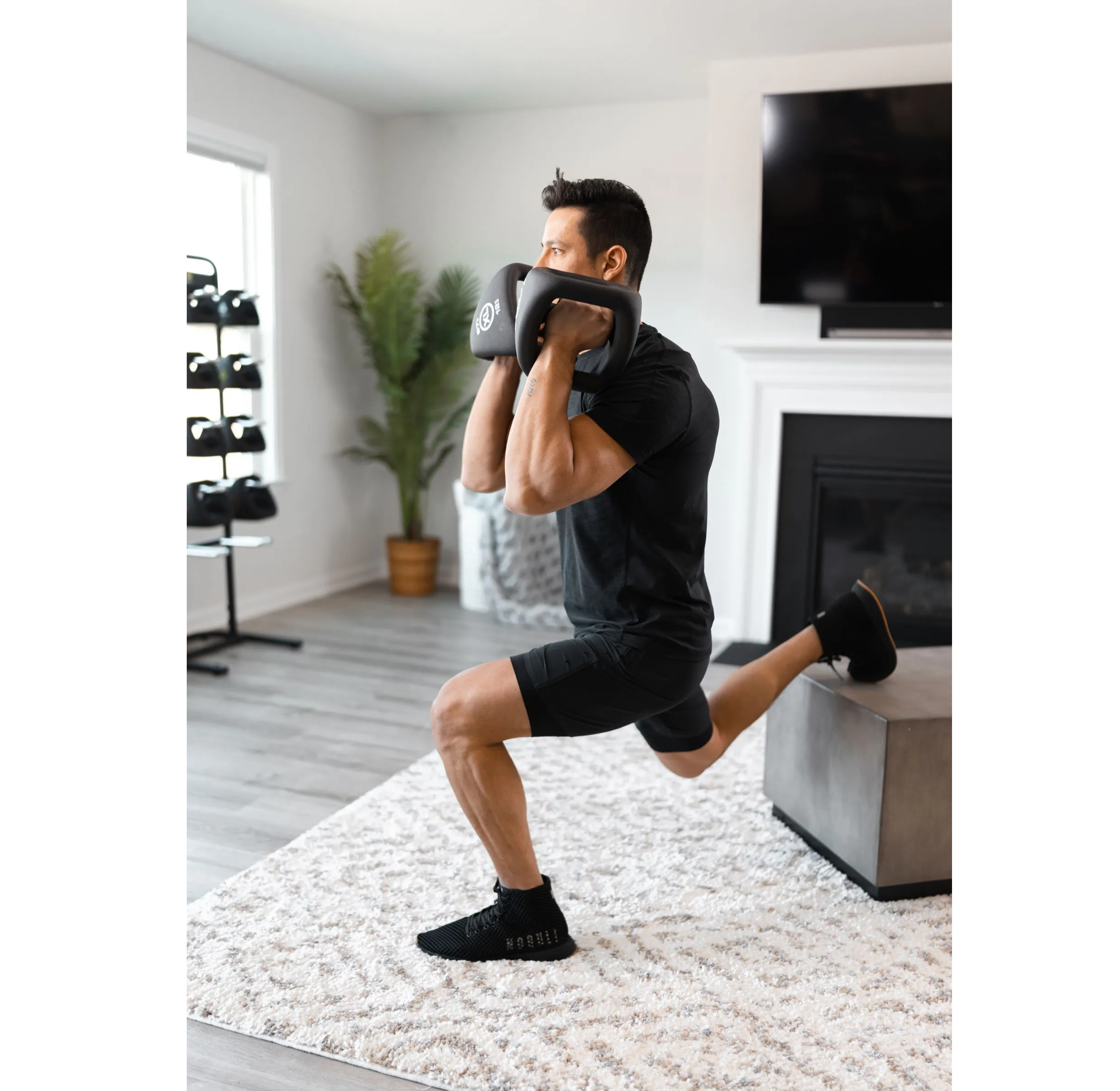 A male athlete performing a Bulgarian split squat in his home gym with YBell Neos.