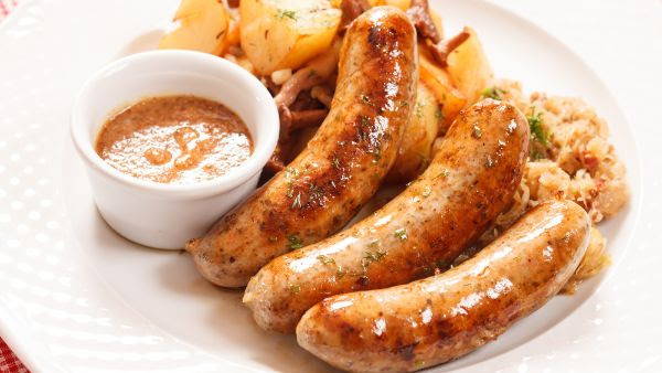 3 sun dried tomato sausages on a plate with sauce and potatoes in the background