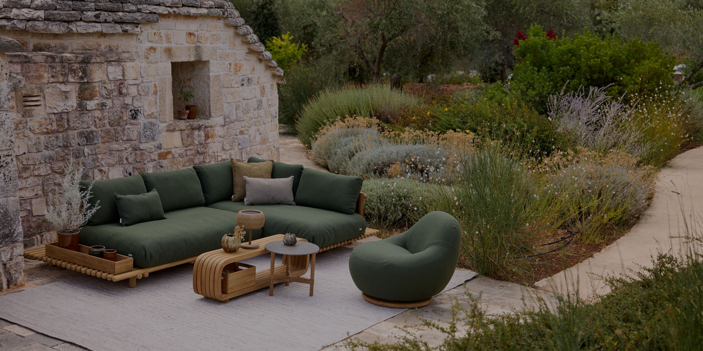 Green outdoor sofa and chair in a lush garden with teak outdoor coffee table