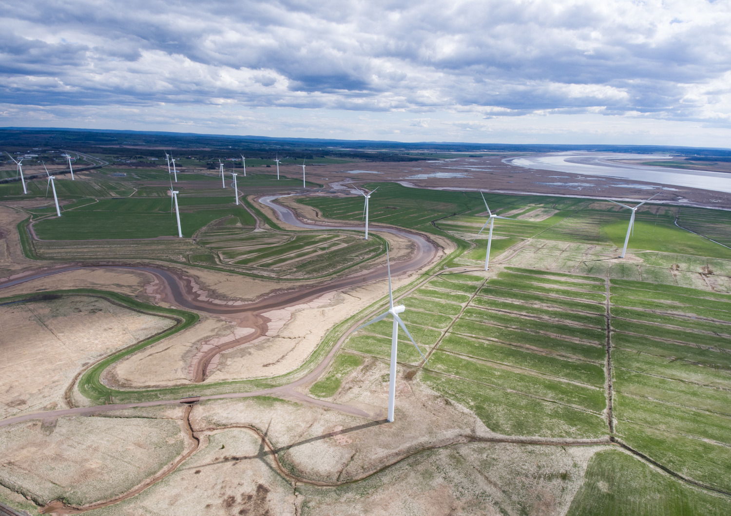 Aerial view of wind turbines in a green landscape with cloudy sky.