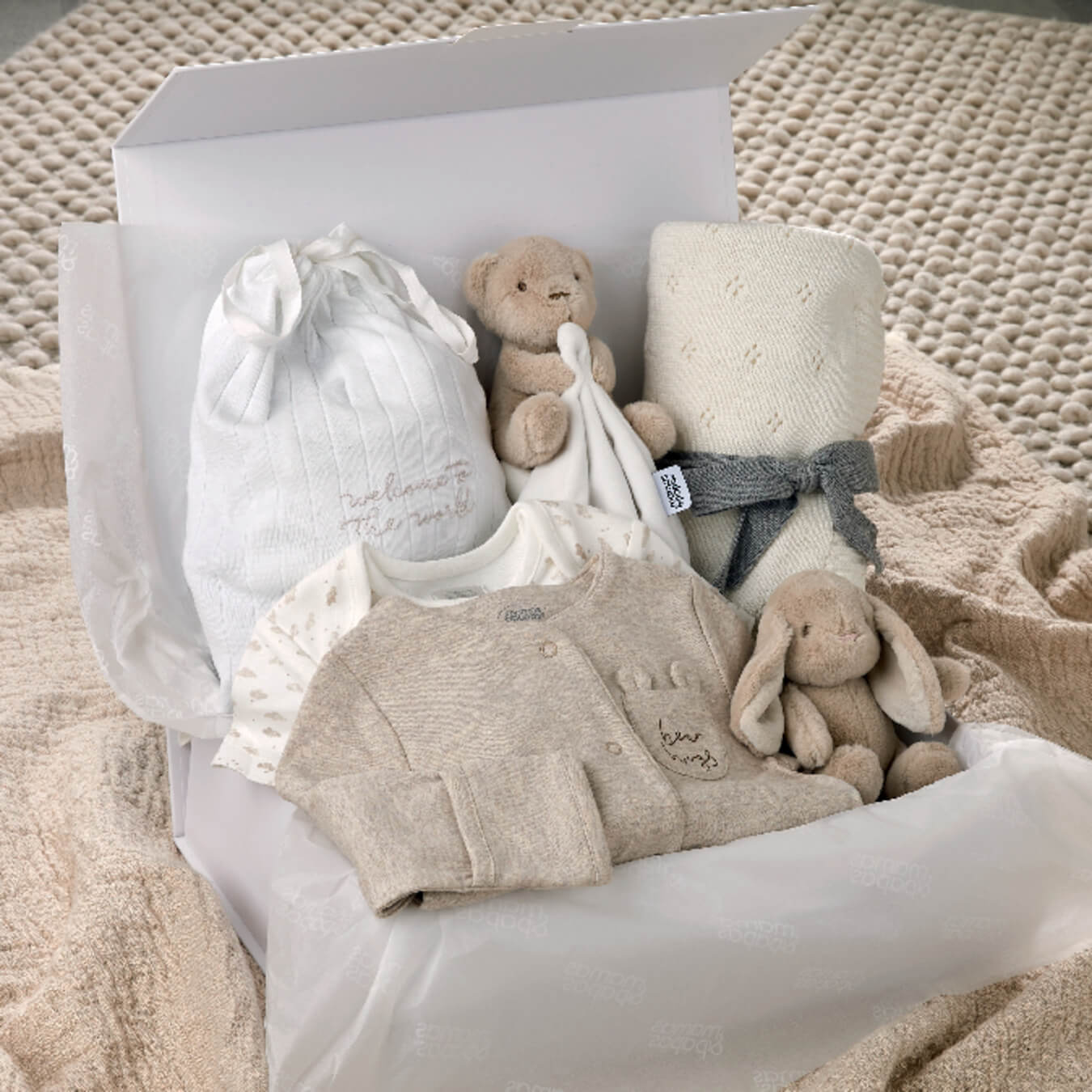 A gift box containing baby clothes, toys, and a blanket.