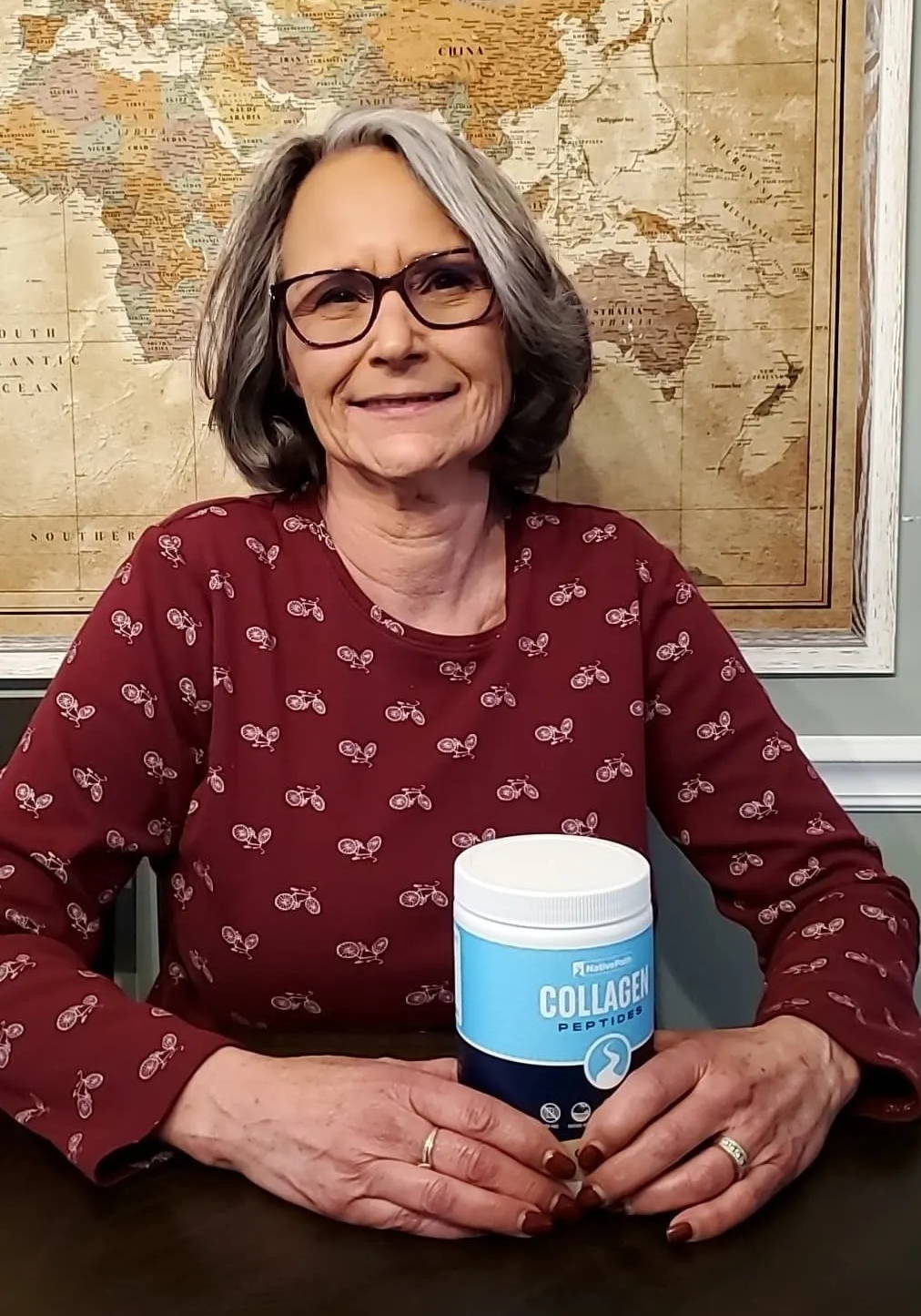 NativePath female customer with gray hair and glasses holding a jar of NativePath Collagen and smiling into camera