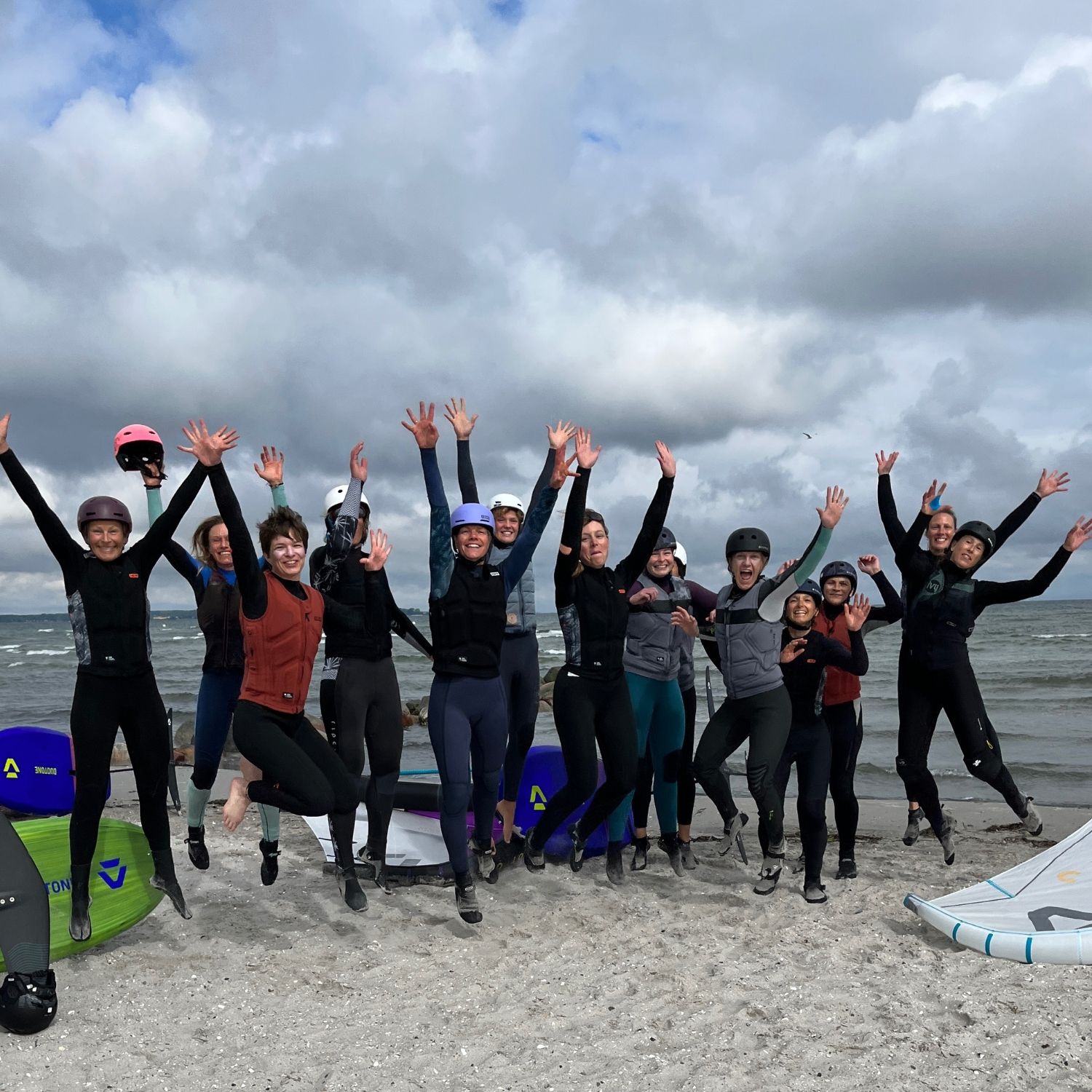 Group of surfers jumping joyfully on the beach with surfboards nearby.