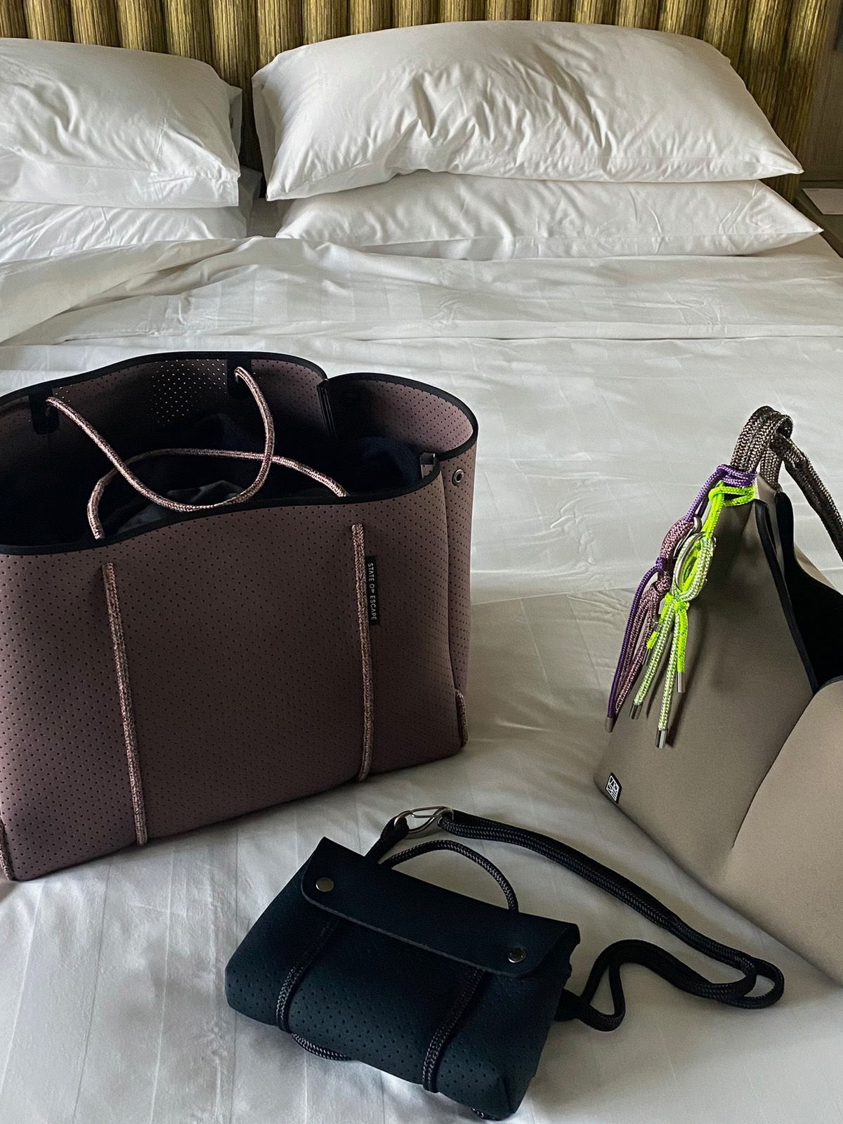 Three handbags on a neatly made bed with white pillows.