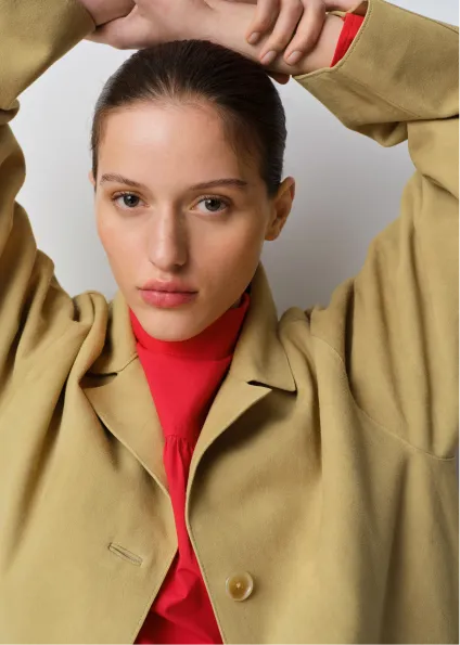 A woman in a beige jacket and red top, posing with arms raised.