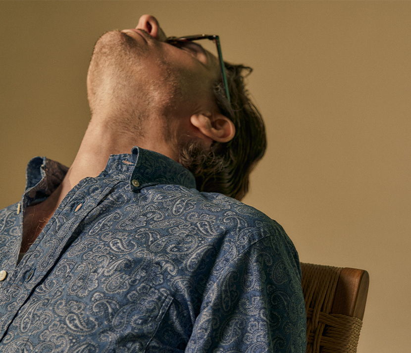 Person leaning back in a chair, looking up, wearing glasses and a patterned shirt.