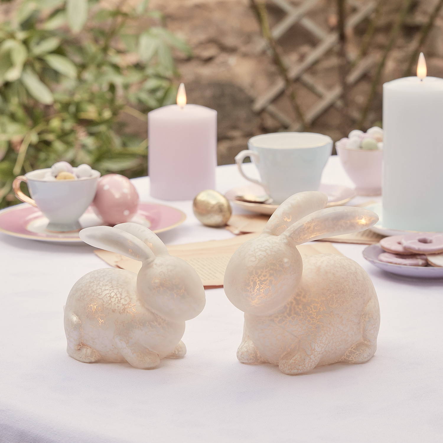 Lot de 2 Décos de Pâques, Lapins Lumineux Blancs en Verre Moucheté sur une table. 