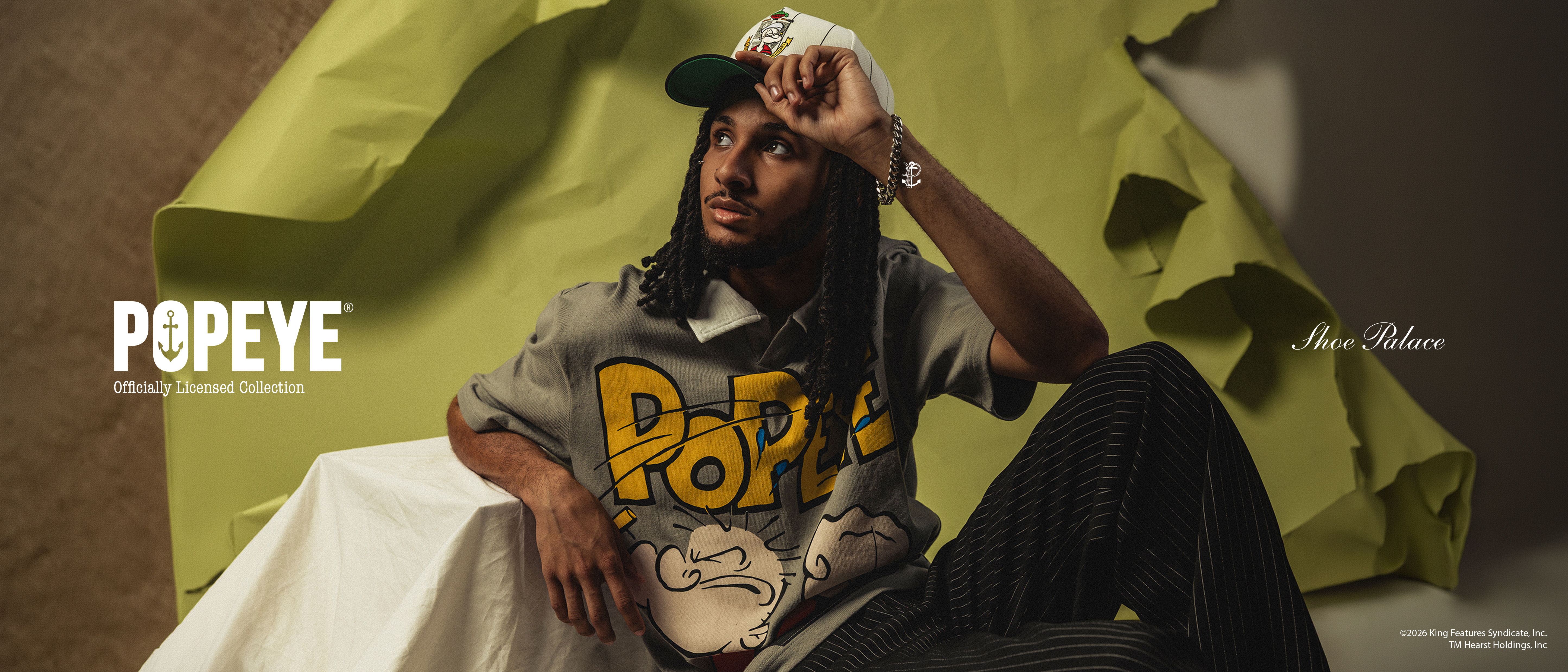 Person wearing a Popeye shirt and cap, posing against green background.